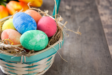 Easter eggs in a basket and tulips on wooden background

