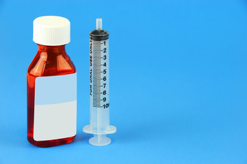 Prescription medicine bottle and oral syringe for baby isolated on blue background