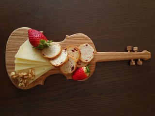  Cheese, strawberry, nuts and crusty bread on wooden cutting board in the form of violin. Top view