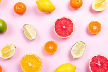 Several kinds of whole and cut citrus on a pink background