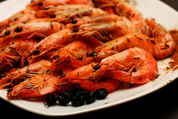 Fresh delicious hot shrimp on a white plate with spices with a lemon on a black table.