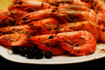 Fresh delicious hot shrimp on a white plate with spices with a lemon on a black table.