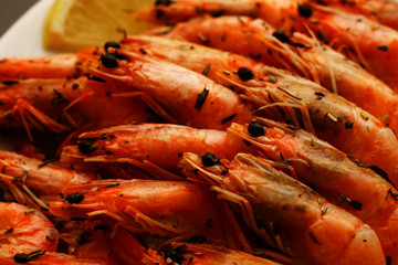 Fresh delicious hot shrimp on a white plate with spices with a lemon on a black table.