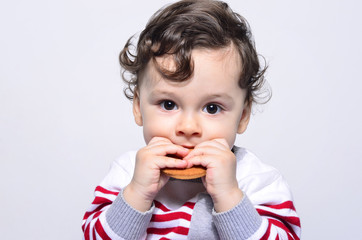Portrait of a cute baby eating a biscuit. One year old kid eating biscuits by himself. Adorable curly hair boy being hungry.