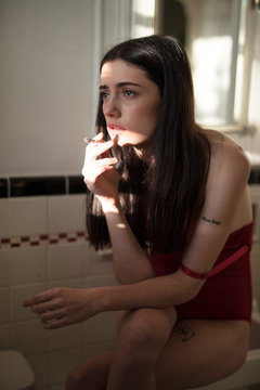 Young woman sitting in bathroom and smoking cigarette