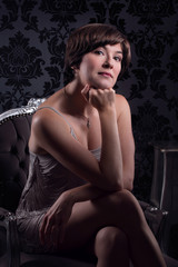 Beautiful young woman wearing silver vintage dress sat on chair.