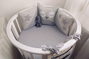 round white baby bed with gray pillows and plush rabbit