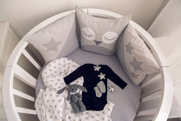 round white baby bed with gray pillows and plush rabbit