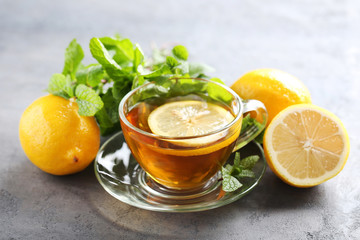 Cup of tea with mint and lemon on grey wooden table