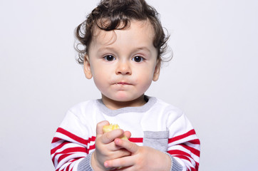 Portrait of a cute baby eating a banana.One year old kid eating fruits by himself. Adorable curly hair boy being hungry.