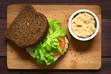 Vegan wholegrain sandwich with celery leaves, tomato, cucumber and chickpea spread or hummus, photographed with natural light (Selective Focus)