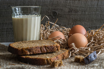 still life with black bread, eggs  on a straw and glass of milk, on old burlup,rustic style .