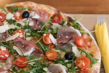 Fototapeta na wymiar Closeup detail of Pizza with prosciutto, cherry tomatoes, grana padano cheese and rucola.