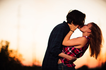 guy and the girl are standing  kissing in the sunset background