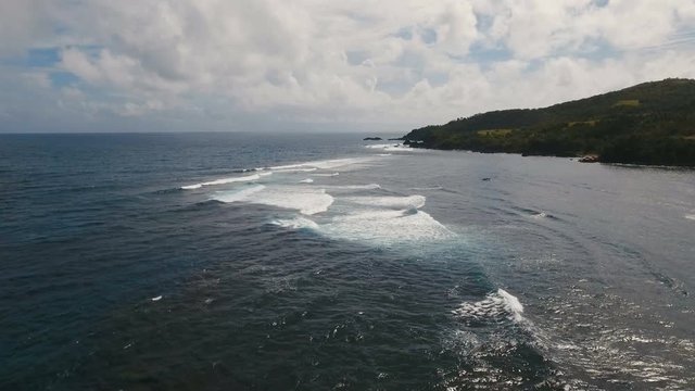 The coast of the tropical island with the mountains and the rainforest on a background of ocean with big waves.Aerial view: sea and the tropical island with rocks, and waves. Seascape: sky, clouds