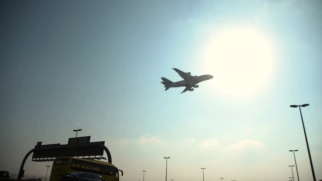 The plane flies low over a busy highway with cars. The plane comes in to land at Dubai Airport and flies low over the road signs.