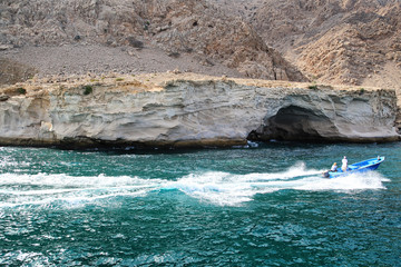 Men on a speedboat passing by a rocks with little cave in Oman
