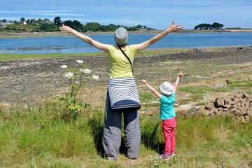 Fototapeta premium Une mère et sa fille expriment leur joie les bras en l'air face à la mer