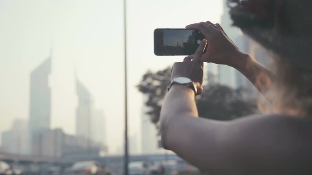 Close-up photographing a mobile phone camera. Female hand pushing on a touch screen and a still image of a skyscraper in Dubai. The horizontal orientation of the mobile screen