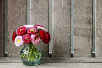 Bouquet of red, pink and white daisies in glass vase. Wooden bac