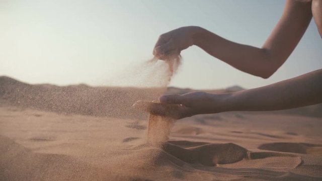 Close-up: girl takes the sand in the palm. Female hand taking up the sand, the sand flies away in the wind. Desert. Time like the sand.