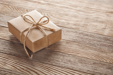 Fototapeta na wymiar Gift box in kraft paper with bow on wooden background