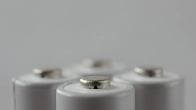 Positive terminals of four batteries slowly rotates on a white background.