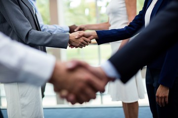 Mid section of business executives shaking hands with each other - obrazy, fototapety, plakaty