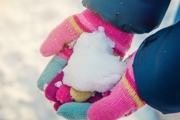 Heart from snow in hands colored knitted gloves.