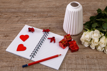 White roses with hearts, gift boxes and vase. Valentines day concept. Red pencil with notebook. Love design. Wooden rustic board.