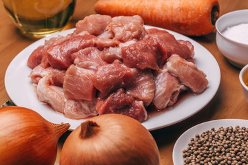 Raw uncooked meat sliced in cubes with vegetables and spices on rustic wood