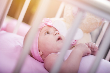 Close up of a beautiful baby girl lying on the bed. Infant lying on a bed. Family morning at home. Happy baby wearing a pink shirt. Newborn kid with toy bear.