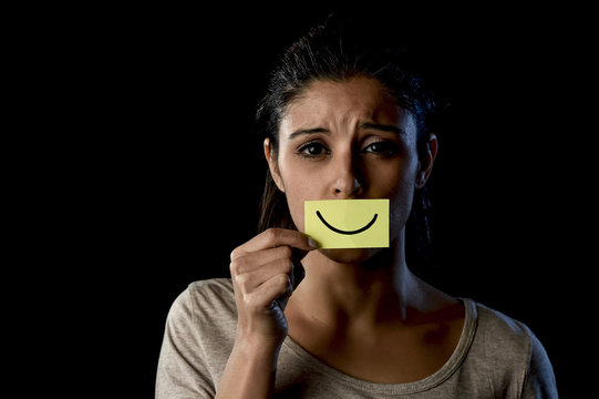  Latin sad depressed latin girl holding paper hiding her mouth behind fake drawn smile