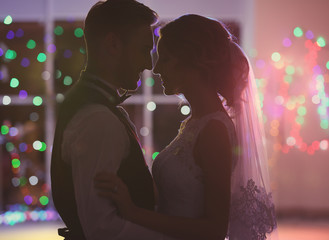 Cute happy wedding couple dancing against defocused lights