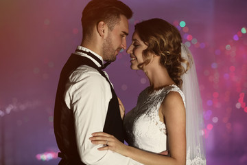 Cute happy wedding couple dancing against defocused lights