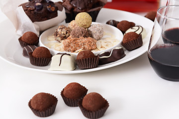 Delicious chocolate candies and red wine on white background