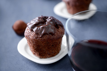 Delicious chocolate muffin and glass of red wine on grey table, close up