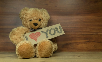 Cute fluffy teddy bear holding a cardboard  I Love You sign, shot on a beautiful wooden surface with enough room for your message