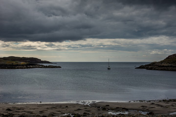Northwest Coast, Scotland - June 6, 2012: Scourie Bay as part of the Atlantic Ocean in the evening during twilight. A sail boat returns to the harbor. Rocky shores and a cloudscape of rain.