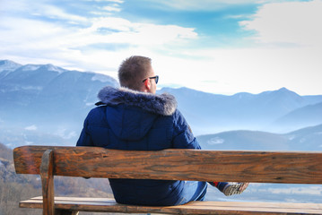 Young man sitting on a bench admiring the mountain view