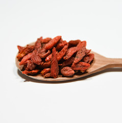 red dried goji berry fruit on decorative wooden spoon on white background close up