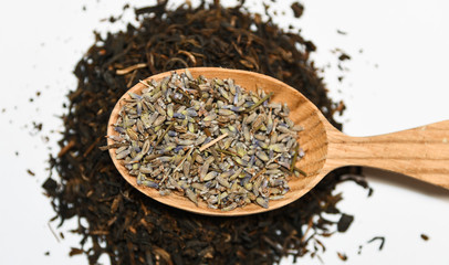 loose dried lavender flowers seeds for infusion or cosmetic use served on a wooden spoon on black tea on white backround