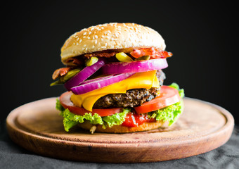 Burger on a wooden table against black background. Selective focus