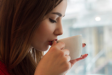  Young girl drinks tea from  smal cup in cafe with big window