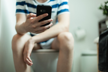 Boy sitting on a toilet using his mobile