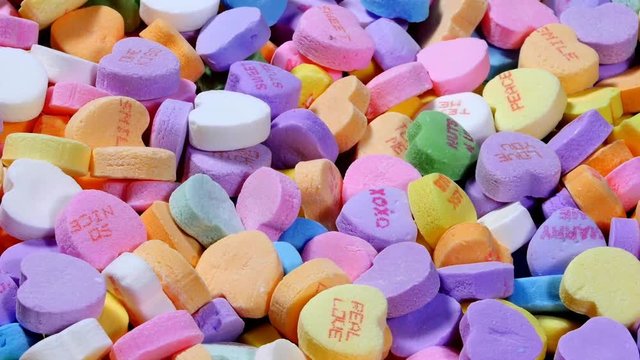 A rotating bowl of sweet Valentines heart shaped candy in various pastel colors and messages of affection.