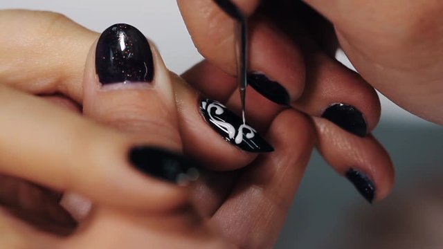 Female manicurist hand applying draw white black on beige nail in beauty saloon, close up white table
