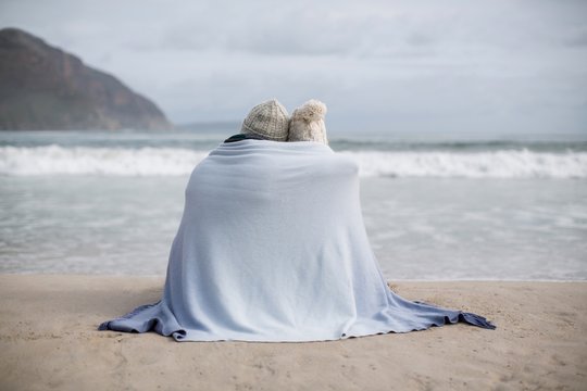 Mature couple wrapped in blanket on the beach - Powered by Adobe