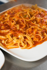Chef serving fettuccine with cheese sauce on a white plate approaching in an Italian food restaurant.