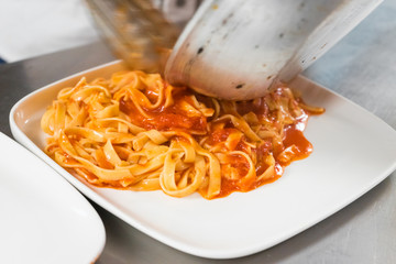 Chef serving fettuccine with cheese sauce on a white plate approaching in an Italian food restaurant.